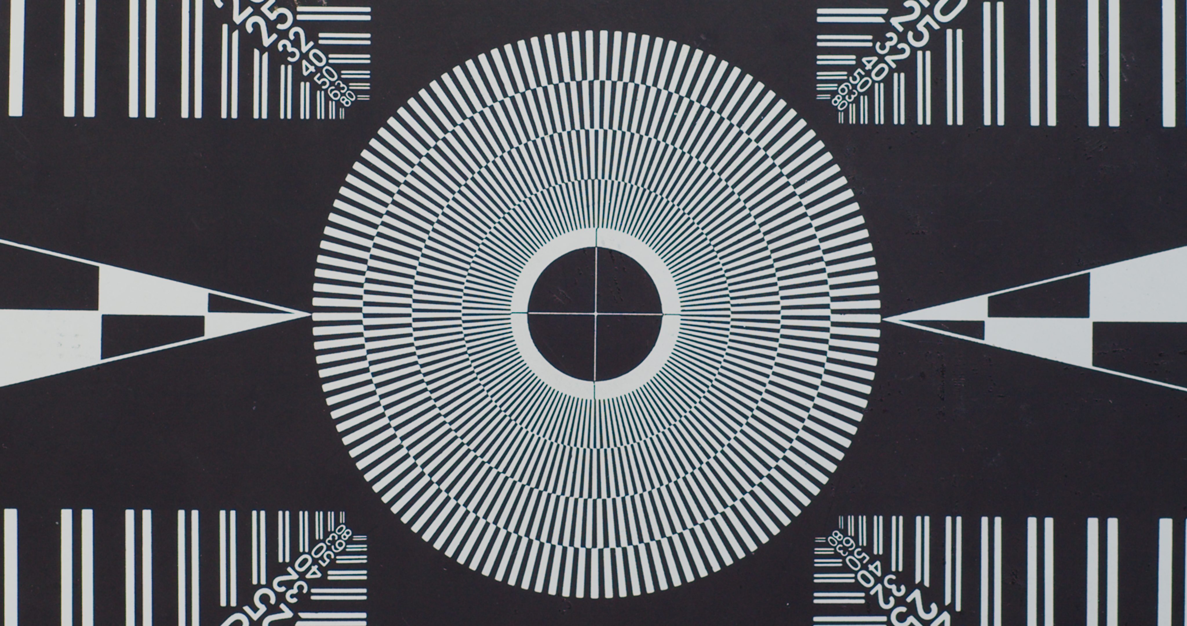 a graphic design featuring concentric circles and radial lines in black and white with triangular shapes and linear patterns at the edges creating a striking visual effect this image serves as a test pattern often used in television broadcasting digital production A graphic design featuring concentric circles and radial lines in black and white, with triangular shapes and linear patterns at the edges, creating a striking visual effect. This image serves as a test pattern often used in television broadcasting.