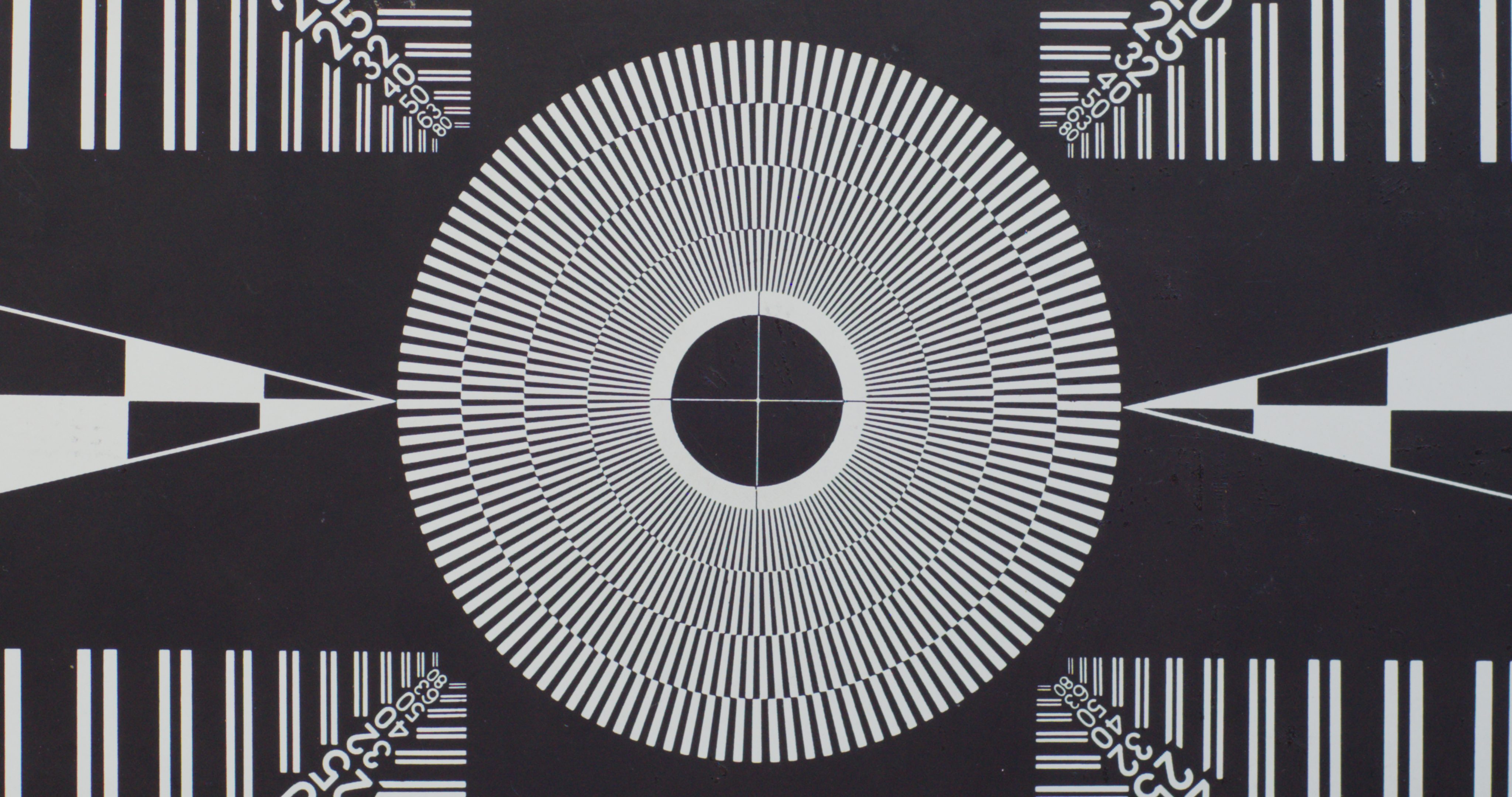 a black and white test chart featuring concentric circles radial lines and various geometric shapes arranged symmetrically around a central circle vertical and horizontal lines create a gridlike pattern on the sides digital production A black and white test chart featuring concentric circles, radial lines, and various geometric shapes, arranged symmetrically around a central circle. Vertical and horizontal lines create a grid-like pattern on the sides.