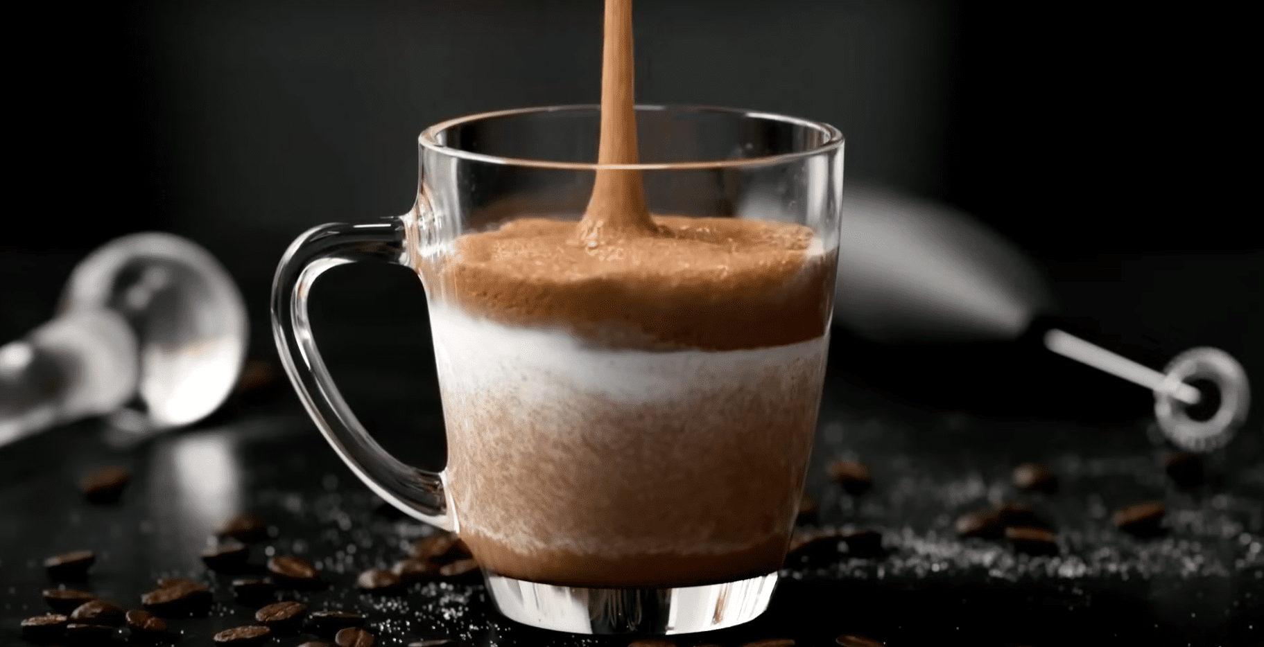 a clear glass cup filled with layers of frothy coffee and cream on a dark background coffee beans and sugar crystals are scattered on the surface around the cup enhancing the rich café ambiance digital production A clear glass cup filled with layers of frothy coffee and cream on a dark background. Coffee beans and sugar crystals are scattered on the surface around the cup, enhancing the rich café ambiance.